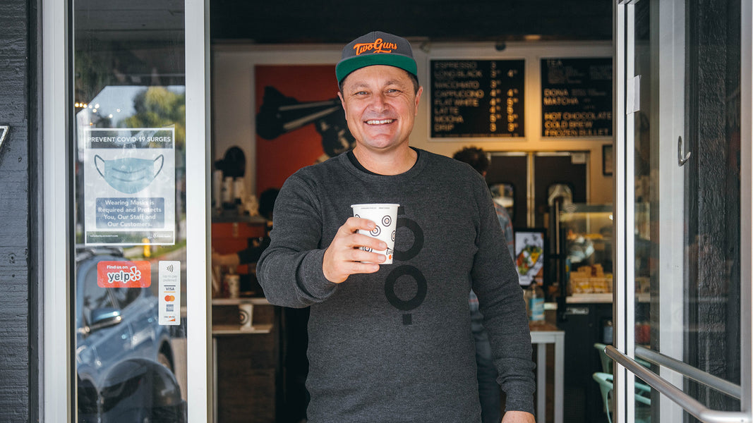 Two Guns Espresso co-founder Stan holding a coffee cup outside busy cafe