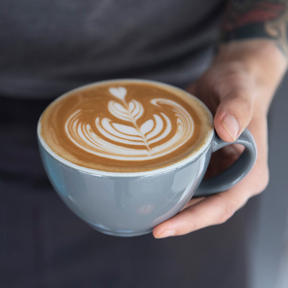 barista holding a grey latte cup with latte art