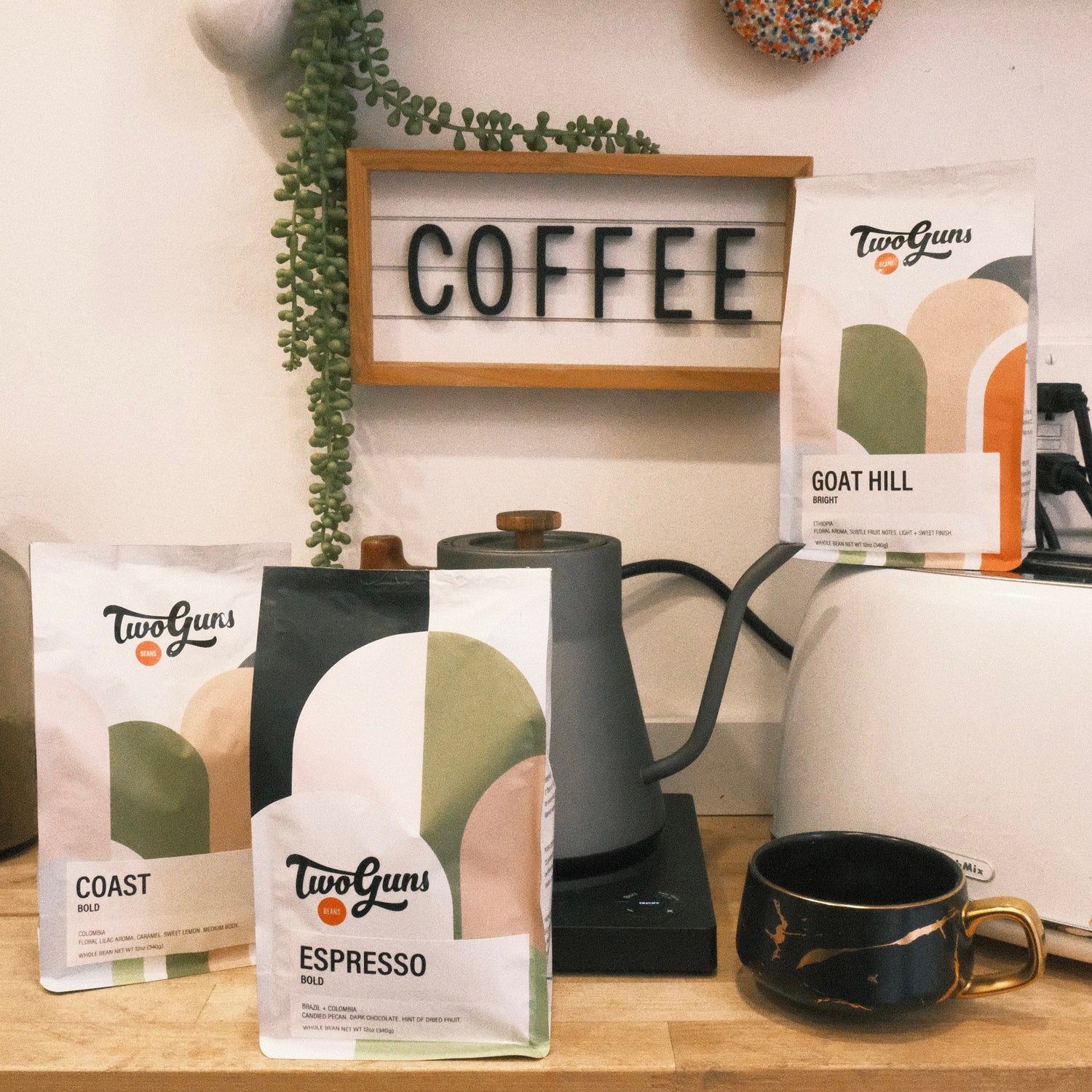 TwoGuns coffee packages on a kitchen counter with a 'COFFEE' sign in the background.