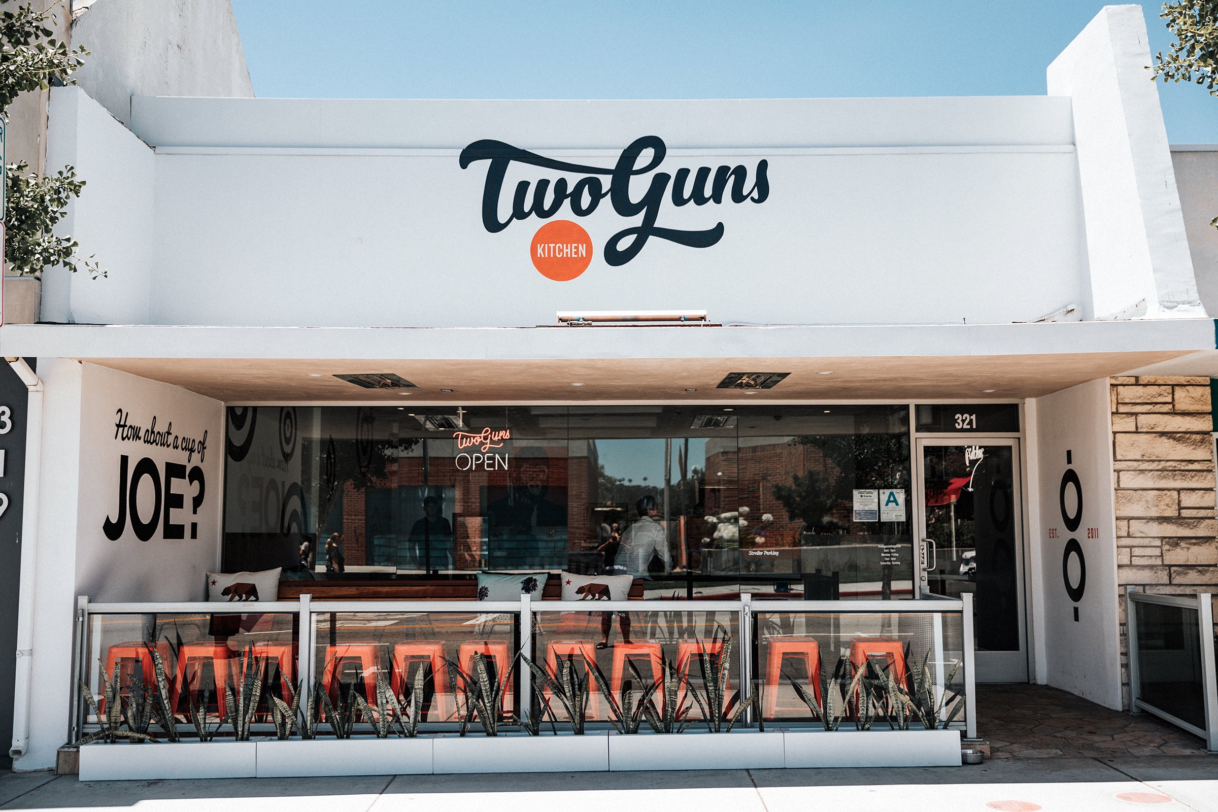 the exterior of two guns el segundo, a white building with a painted sign and outdoor seating