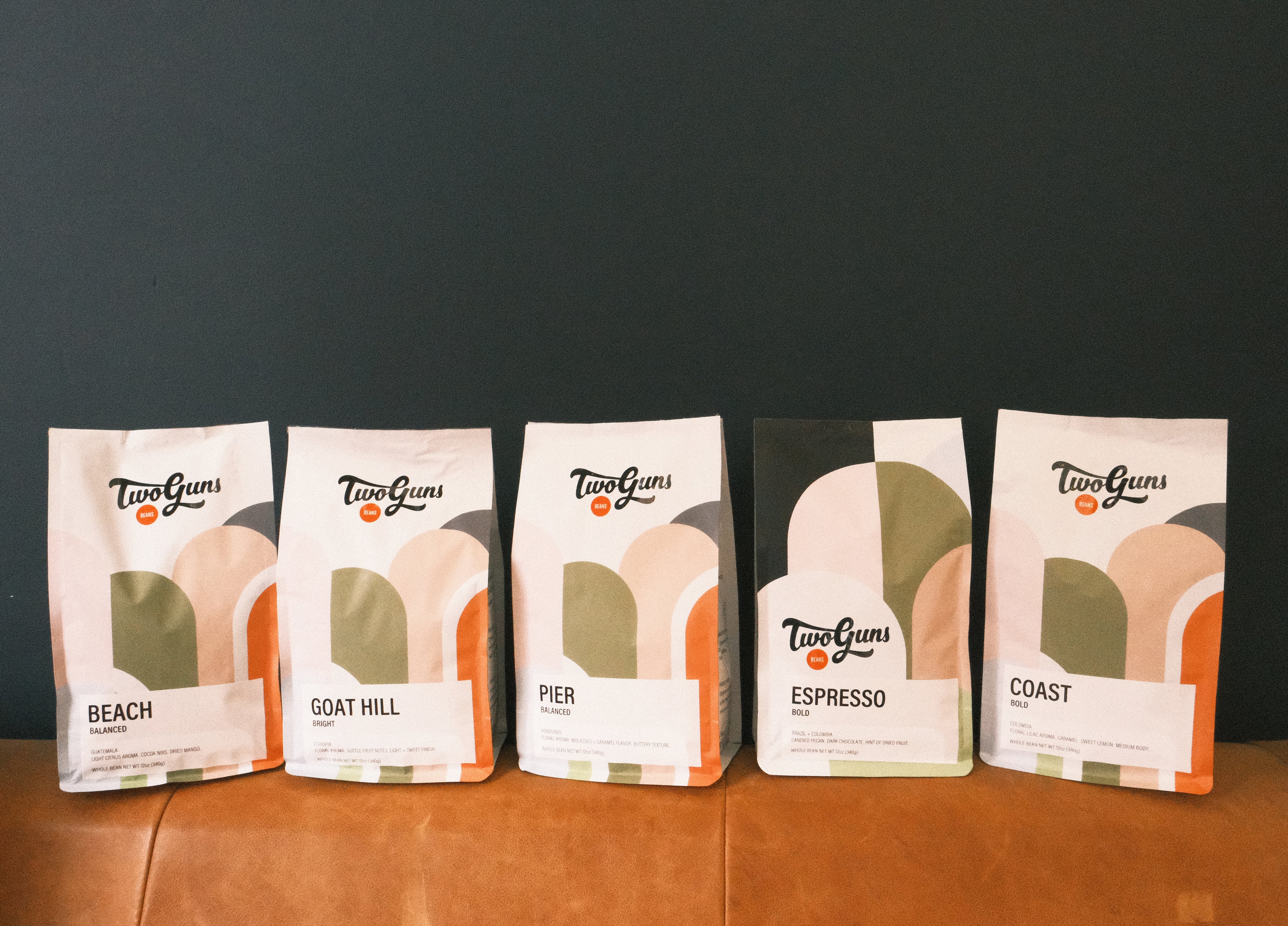 Five packages of 'Two Guns' coffee on a wooden surface with a dark background