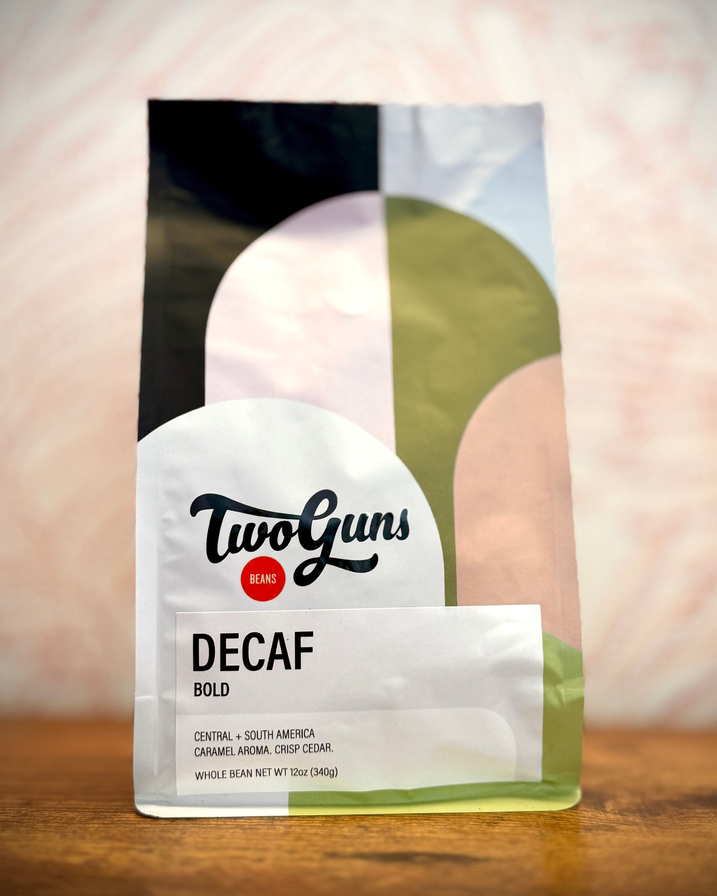 Two Guns Decaf Bold coffee package on a wooden surface with a blurred background