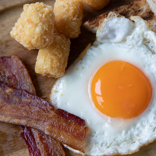 close up of sunny-side up egg, bacon and tots