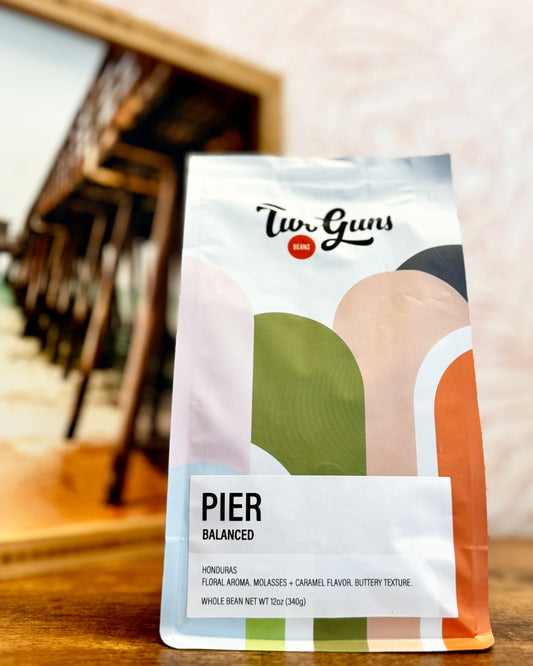 Coffee bag labeled 'Two Guns' with 'Pier Balanced' flavor on a wooden surface.